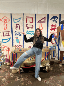 a woman stands in front of a wall with egyptian writing