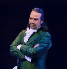 a man in a green suit with his arms crossed is standing on a stage .