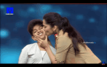 a woman kisses a young boy on the cheek in front of a mallemala tv screen