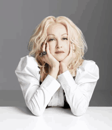 a woman with blonde hair and a white shirt is sitting with her hands on her face