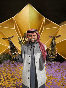 a man holding two awards in front of a sign that says " awa "