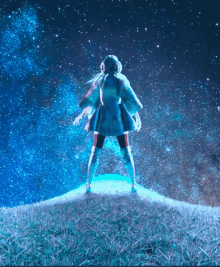 a woman standing on top of a grassy hill looking up at the stars