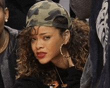 a woman wearing a camouflage hat and hoop earrings is sitting in a crowd .