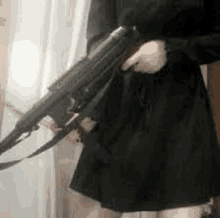 a woman in a black dress is holding a rifle .