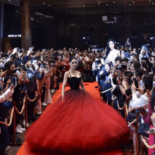 a woman in a red dress is walking down a red carpet in front of a crowd of people