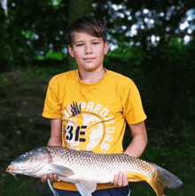 a young boy holding a large fish wearing a yellow shirt that says predators