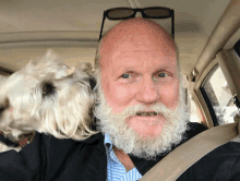 a bald man with a beard is holding a small white dog on his shoulder