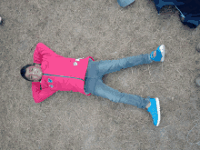 a young boy wearing a pink adidas jacket is laying on the grass