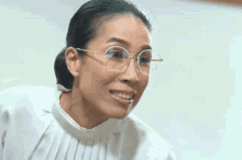 a woman wearing glasses and a white top smiles