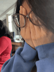 a girl wearing glasses covers her face with her hands