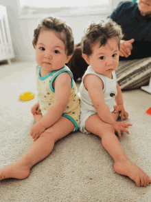 two babies are sitting next to each other on the floor and one of them has a shirt with a bear on it