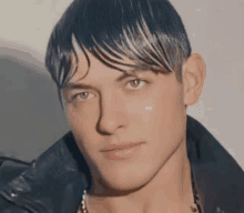 a close up of a man 's face with wet hair and a leather jacket .