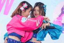 two girls in pink and blue jackets are hugging each other .