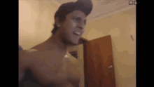 a shirtless man wearing a hat is standing in front of a door in a room .