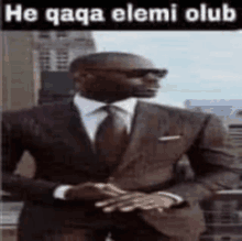 a man in a suit and tie is standing in front of a building with a caption that says he qaqa elemi club .