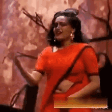 a woman in a red saree is dancing in front of a wall .