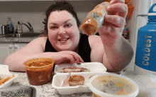 a woman is sitting at a table with containers of food and a blue water bottle that says coldest on it