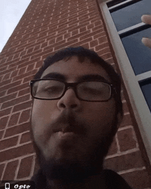 a man wearing glasses is smoking a cigarette in front of a brick building