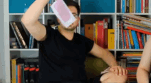 a man in a black shirt throws a piece of paper in the air in front of a bookshelf with books on it