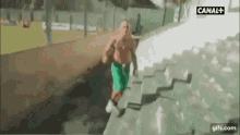 a shirtless man in green shorts is running down a set of stairs in front of a canal + sign