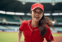 a woman in a red baseball uniform and hat smiles for the camera