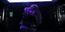 a woman wearing a purple leather jacket with studs on the back is standing in an elevator .