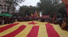 a group of people are sitting in front of a large yellow and red flag with a star on it .