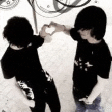 two young men are making a heart shape with their hands in a black and white photo .