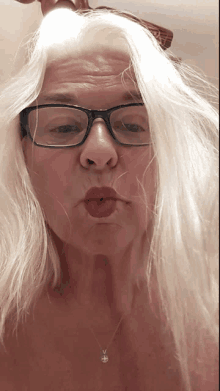 a woman wearing glasses and a necklace blows a kiss