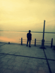 a man in a hat stands on a dock looking out over a body of water