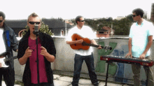 a man singing into a microphone while a man playing a guitar and another man playing a keyboard