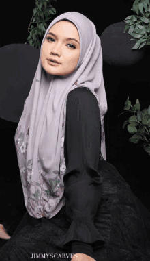 a woman wearing a gray hijab and a black shirt with jimmyscarves written on the bottom