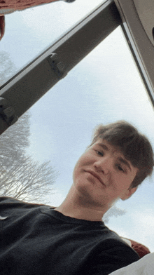 a young man in a black shirt is looking up at the sky through a window