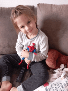 a little girl sitting on a couch holding a toy spiderman