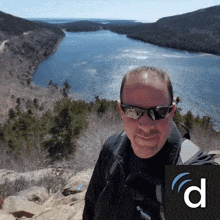 a man wearing sunglasses is standing on top of a mountain overlooking a river