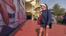 a woman wearing a blue jacket and a white visor stands in front of a large wall with a picture of a woman on it