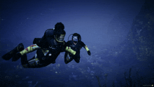 two scuba divers are swimming in the ocean and one of them is wearing a rescue suit