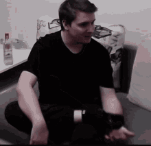 a man in a black shirt is sitting on a couch with his hands on his knees .