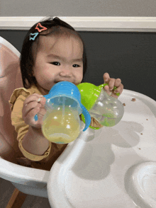 a baby sitting in a high chair drinking from a cup