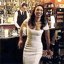 a woman in a white dress is walking in a bar .