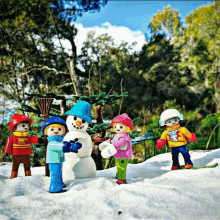 a group of playmobil figures are standing around a snowman in the snow