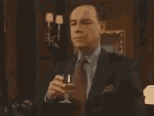 a man in a suit and tie is drinking a glass of wine in a dark room .