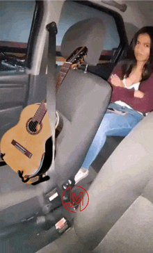 a woman sits in the back seat of a car with a guitar hanging from the back seat belt