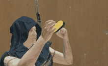 a man in a blue hood holds a gun and looks at a corn on the cob