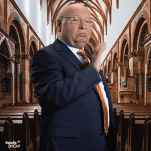 a man in a suit and tie stands in a church with the words heute show on the bottom right