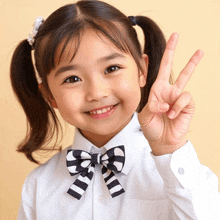 a little girl wearing a bow tie and a white shirt is giving a peace sign