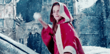 a girl in a red cape is throwing a snowball in the air