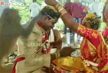 a bride and groom are getting married and the bride is putting a veil on the groom 's head .