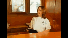 a woman in a white t-shirt with the word hawaii on it is standing at a counter holding a clipboard .