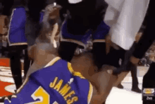 a basketball player in a purple jersey is kneeling down on the floor .